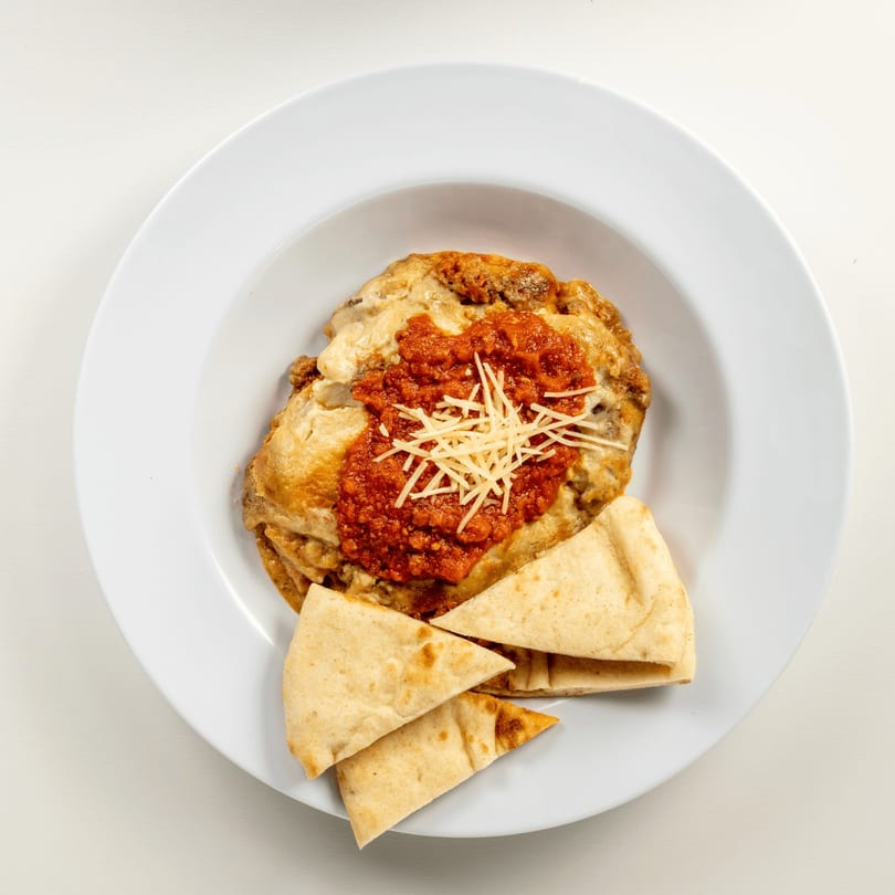 Greekos Grill & Cafe moussaka with red sauce, shredded cheese, and pita bread on a white plate.