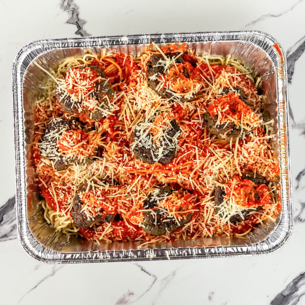 Spaghetti and meatballs with red sauce and shredded cheese in a large aluminum pan.