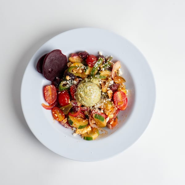 Colorful salad with cherry tomatoes, cucumbers, red onions, and a scoop of green pesto.