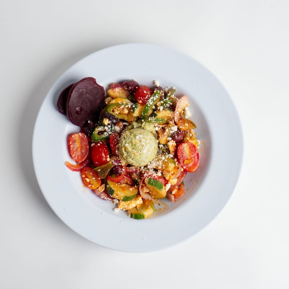 Colorful salad with cherry tomatoes, cucumbers, red onions, and a scoop of green pesto.