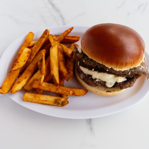 A double cheeseburger with melted white cheese and a side of seasoned fries on a white plate.