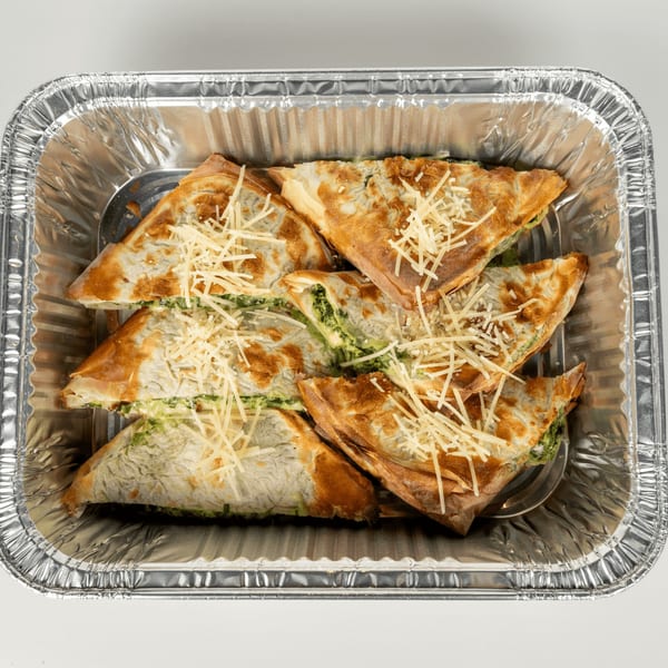 Spanakopita triangles with golden crusts and shredded cheese in a silver foil container.