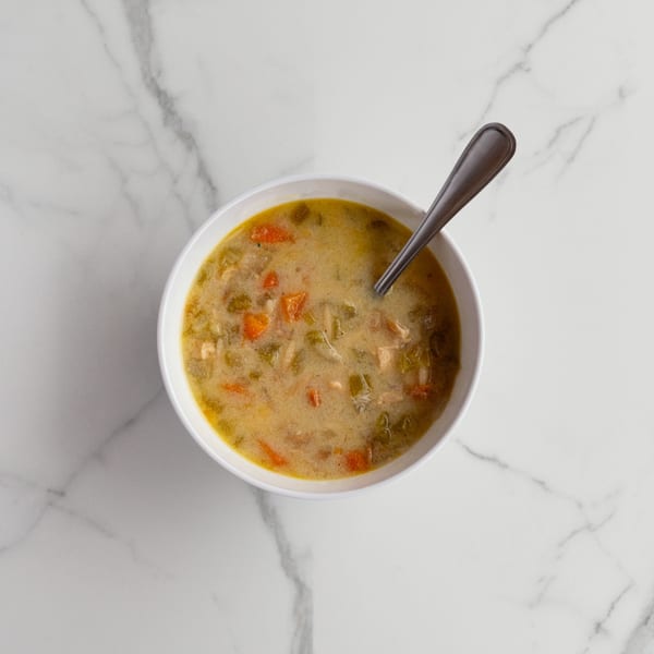 Overhead view of a white bowl filled with creamy chicken and vegetable soup, with a spoon.