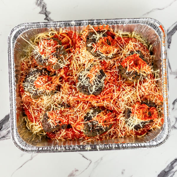 Spaghetti and meatballs with red sauce and shredded cheese in a large aluminum catering pan.