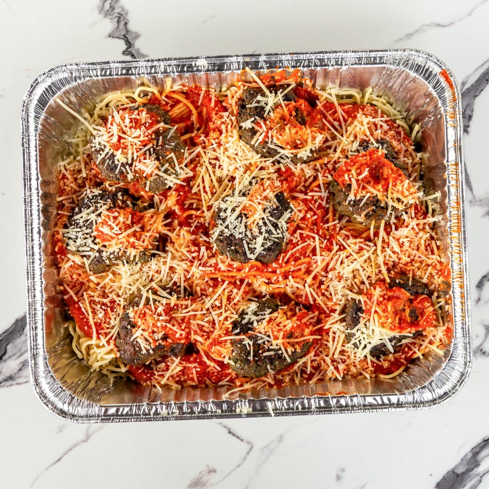 Spaghetti and meatballs with red sauce and shredded cheese in a large aluminum catering pan.