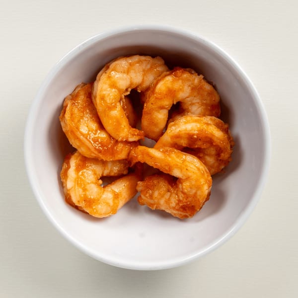 A white bowl filled with several cooked, orange-glazed shrimp, ready to be served at Greekos Grill & Cafe.