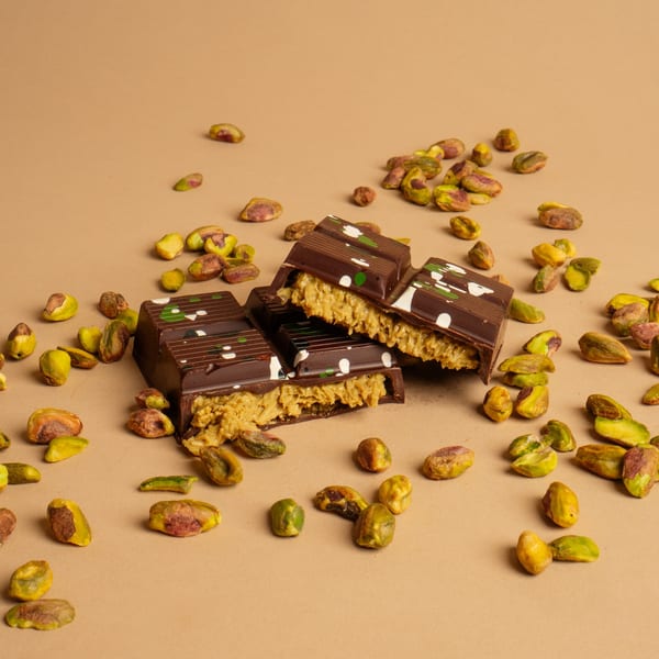Chocolate bars with pistachio filling and decorative white and green dots, surrounded by loose pistachios.