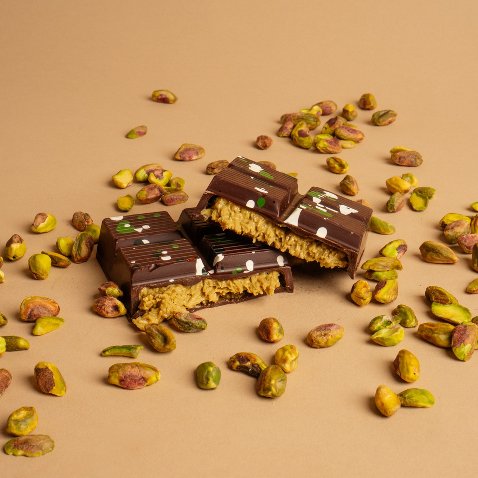 Chocolate bars with pistachio filling and decorative white and green dots, surrounded by loose pistachios.