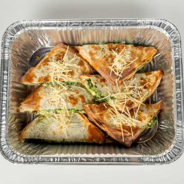 Spanakopita triangles with spinach and cheese filling, topped with shredded cheese in a foil pan.
