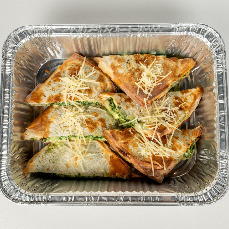 Spanakopita triangles with spinach and cheese filling, topped with shredded cheese in a foil pan.