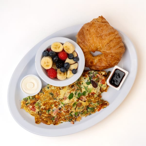 A breakfast plate with a vegetable omelet, fruit salad, croissant, and two dipping sauces.