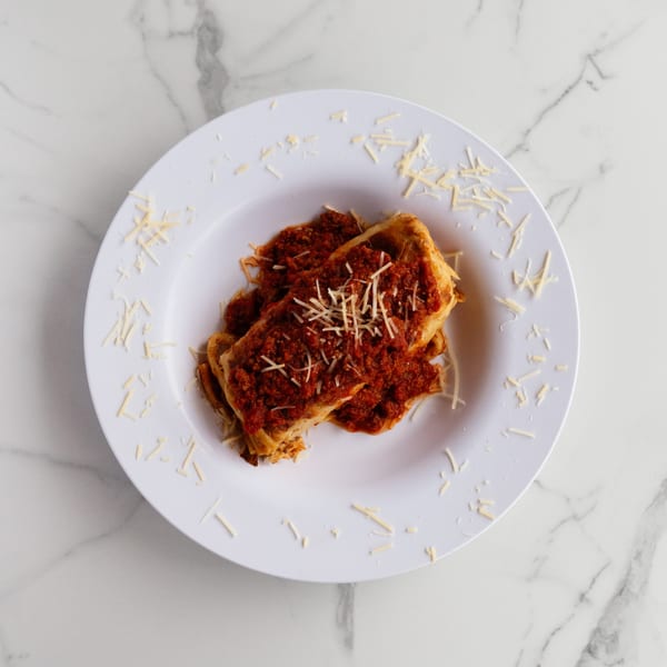 Two pieces of lasagna topped with red sauce and shredded cheese on a white plate.