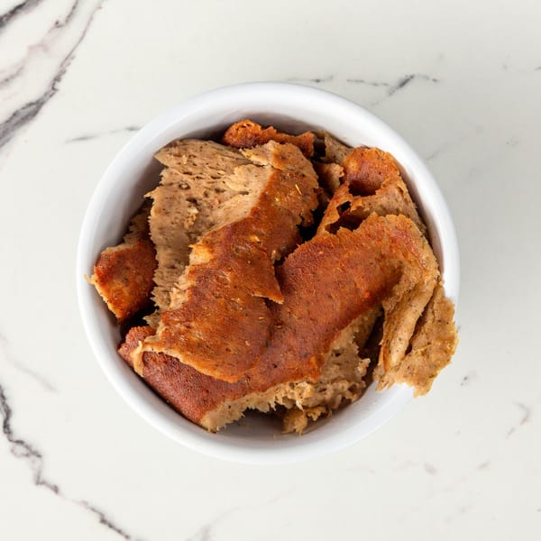 Top-down view of a white bowl filled with pieces of golden-brown, seasoned vegan gyros meat.