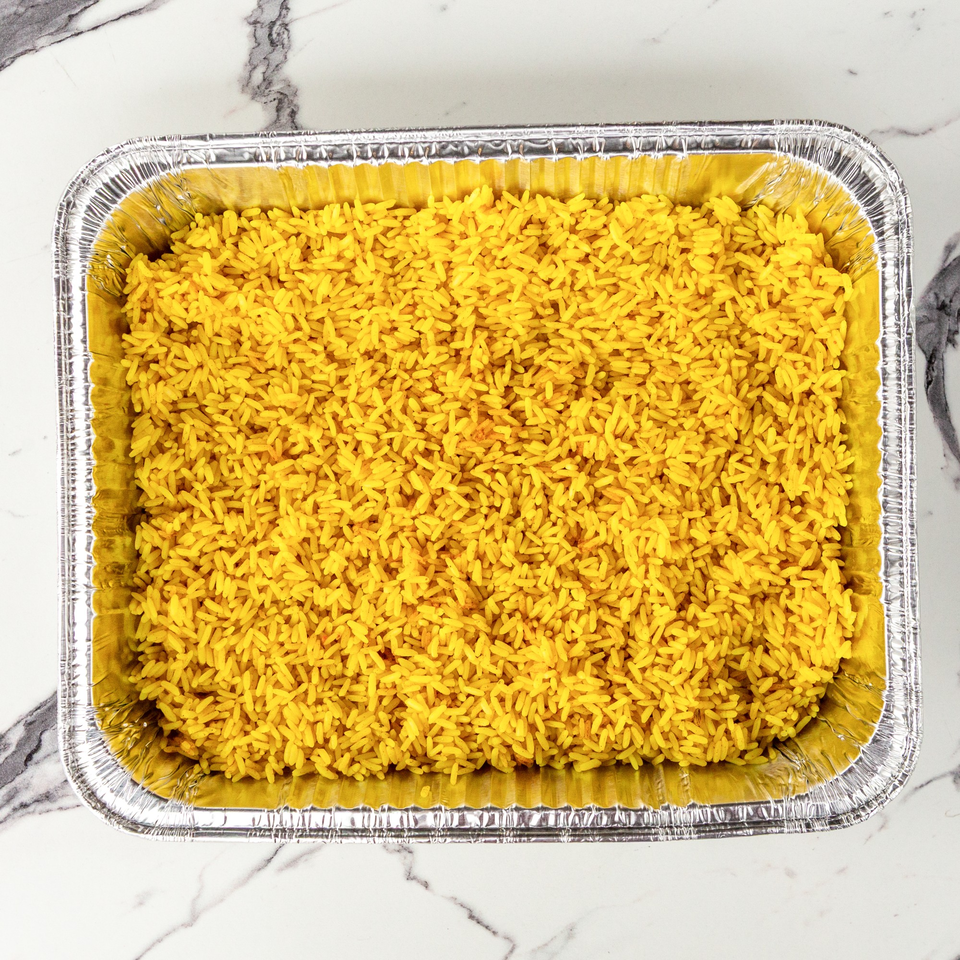 Bright yellow rice fills a rectangular aluminum foil pan, centered on a white marble surface.