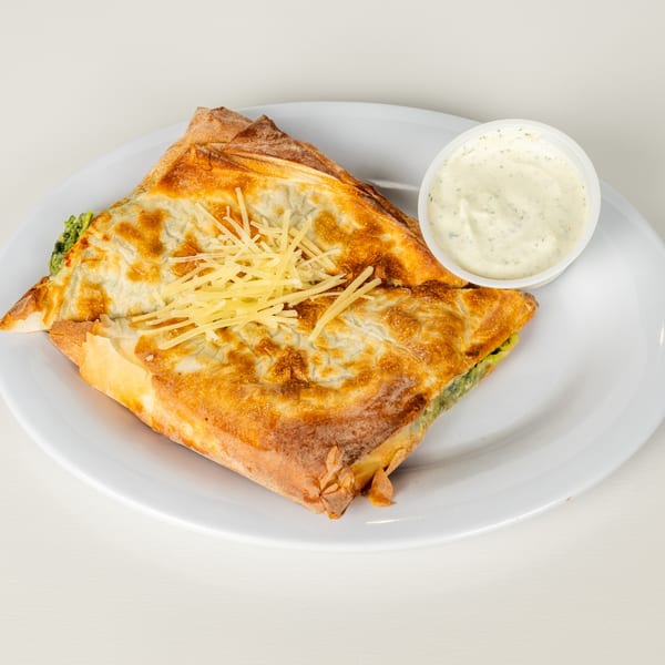 Golden-brown Greek spanakopita with shredded cheese and a side of tzatziki sauce on a white plate.