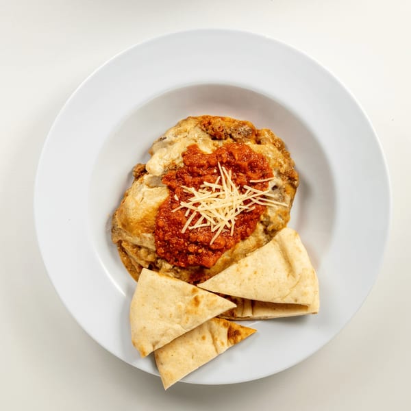 Greekos Grill & Cafe's moussaka topped with red sauce and shredded cheese, served with pita bread.