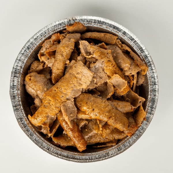 Close-up overhead view of Greek gyro meat slices in a round aluminum takeout container.