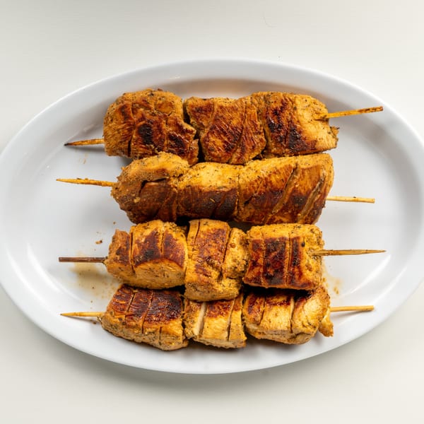 Four skewers of grilled chicken souvlaki on a white oval plate.